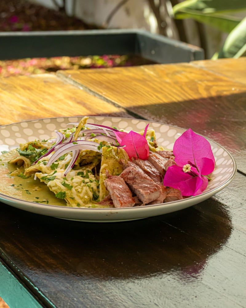 Platillo de carne con ensalada y una flor sobre la mesa